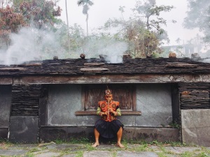 Tribal warriors play the nose flute in front of a slate house